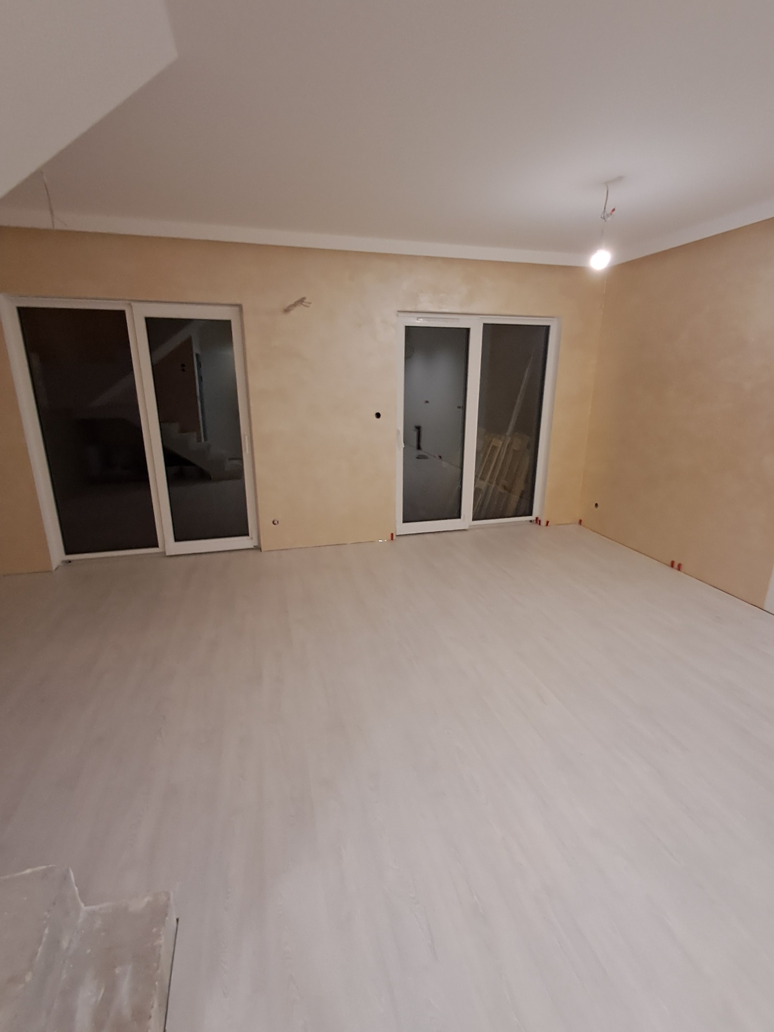 Jasne wnętrze po remoncie: kremowe ściany z efektem dekoracyjnym, białe listwy przypodłogowe i panele podłogowe. Dwa okna balkonowe w białych ramach.