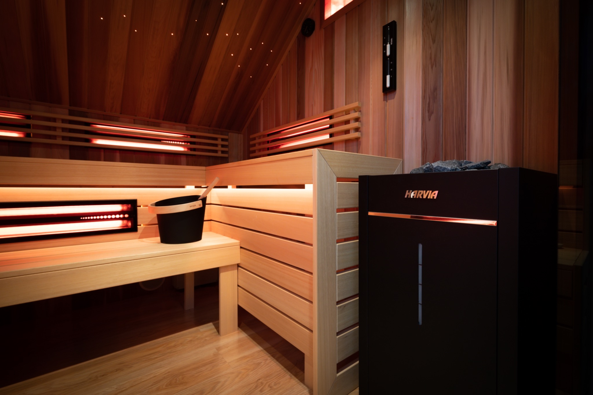 Wnętrze drewnianej kabiny z piecem Harvia, oświetleniem LED w suficie i akcesoriami, takimi jak wiadro z chochlą.