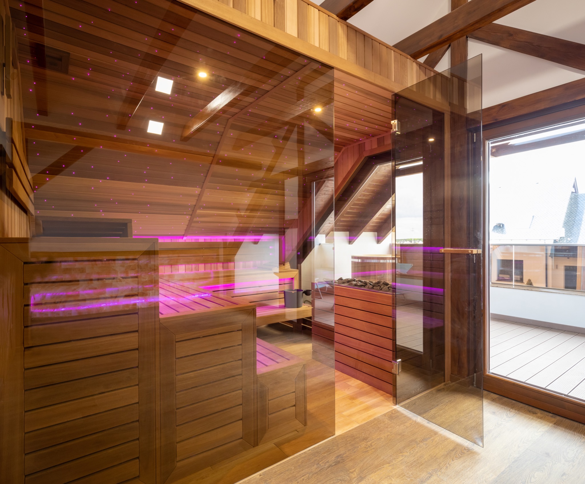 Nowoczesna drewniana kabina z przeszklonymi drzwiami i podświetleniem LED w kolorze fioletowym, widok na balkon.