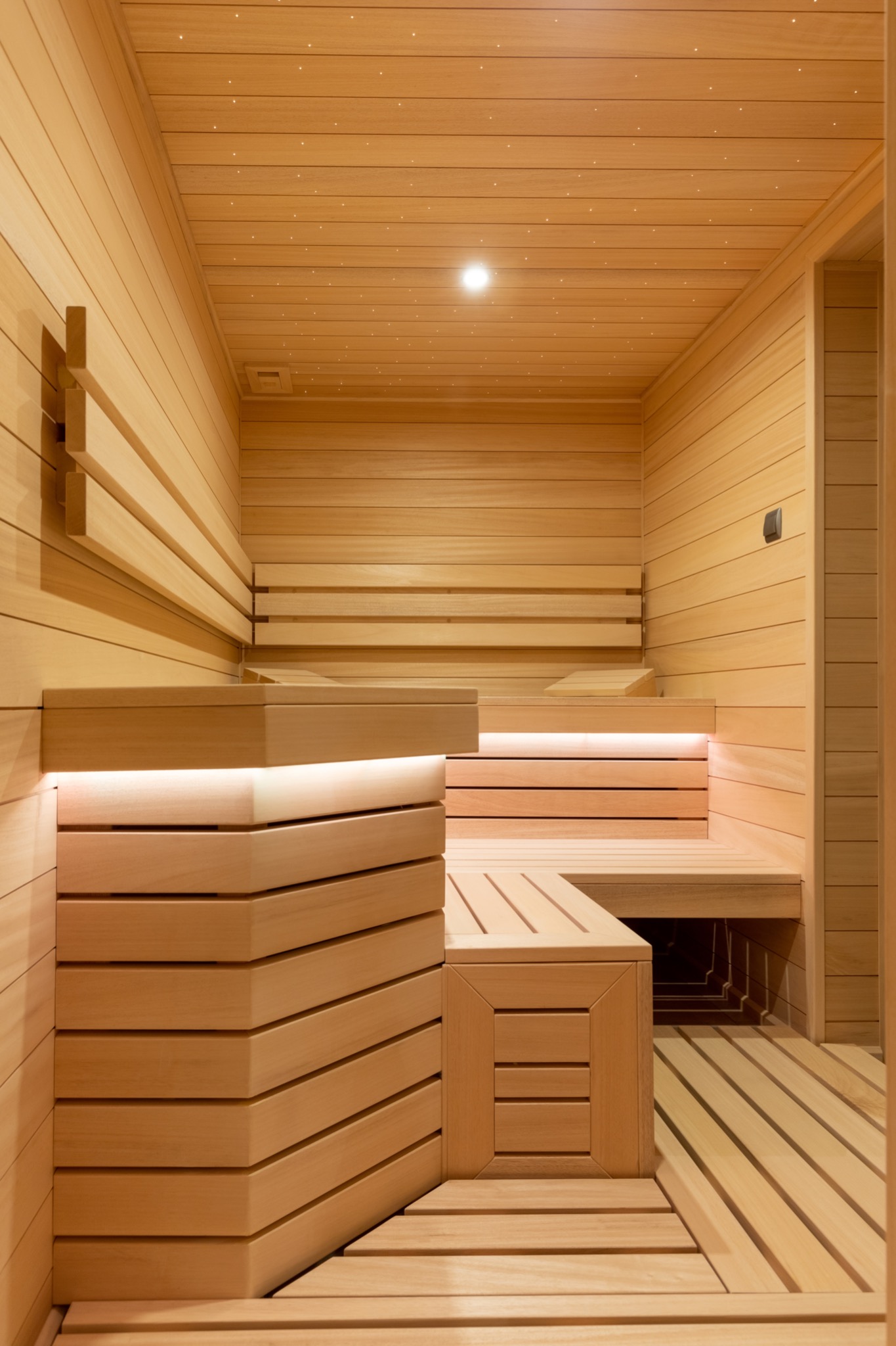 Wnętrze nowej, jasnej sauny z drewna, z podświetlanymi ławkami i dekoracyjnym oświetleniem sufitowym imitującym gwiazdy.