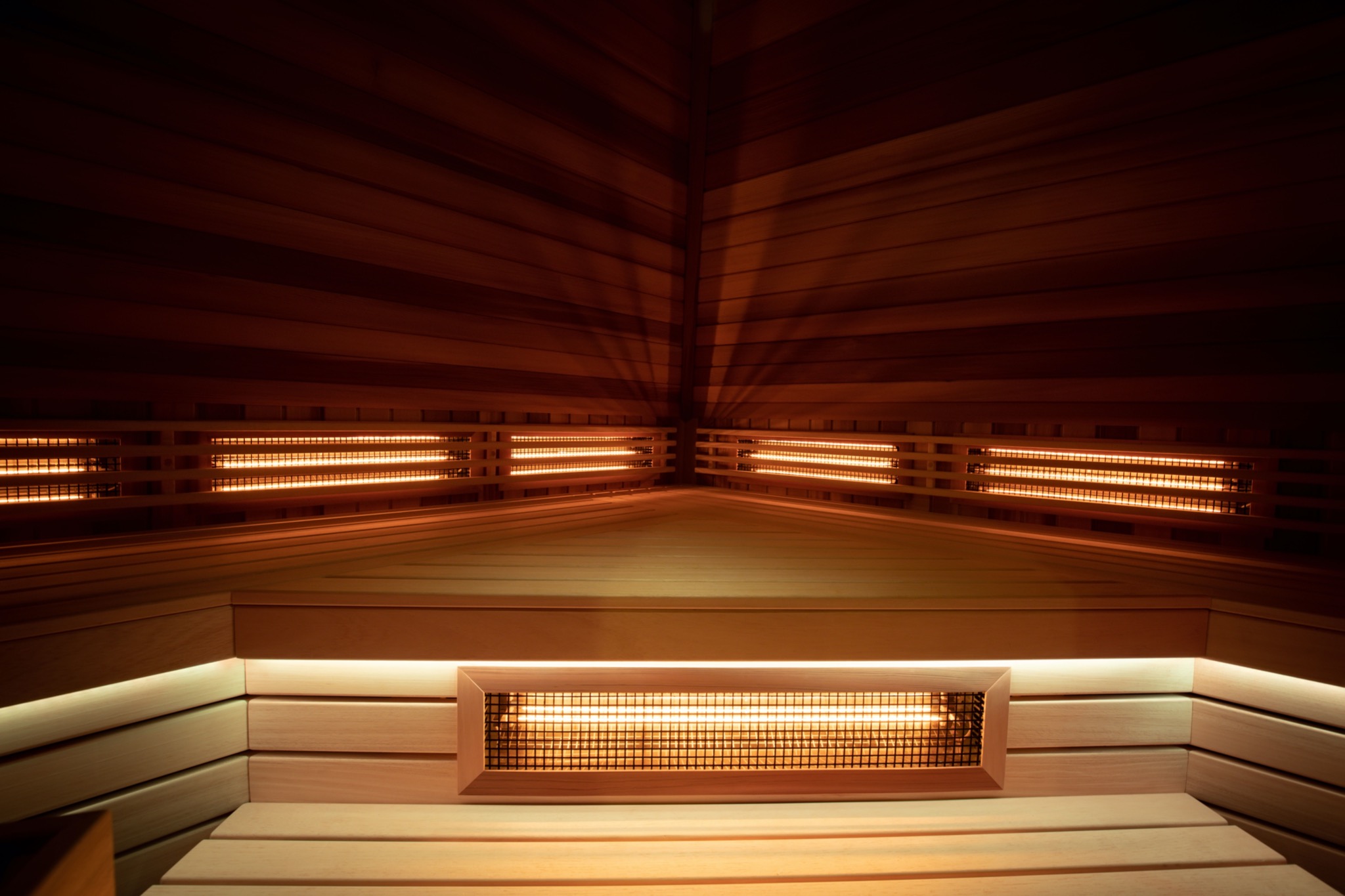 Wnętrze kabiny z drewnianymi panelami, oświetleniem LED i grzejnikami na podczerwień, widok z dołu na sufit w ciepłym oświetleniu.