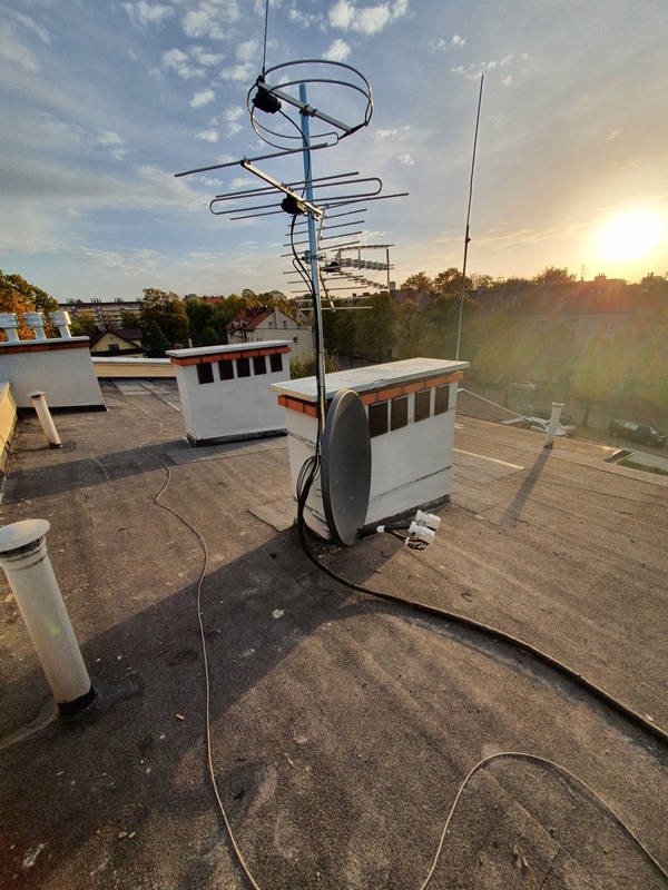 Anteny telewizyjne i satelitarne zamontowane na dachu budynku, widok z góry, zachodzące słońce w tle.