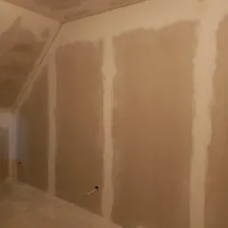 Ściana poddasza po szpachlowaniu płyt karton gips, widoczne łączenia wzmocnione taśmą i zaszpachlowane, przygotowane do dalszych prac wykończeniowych.