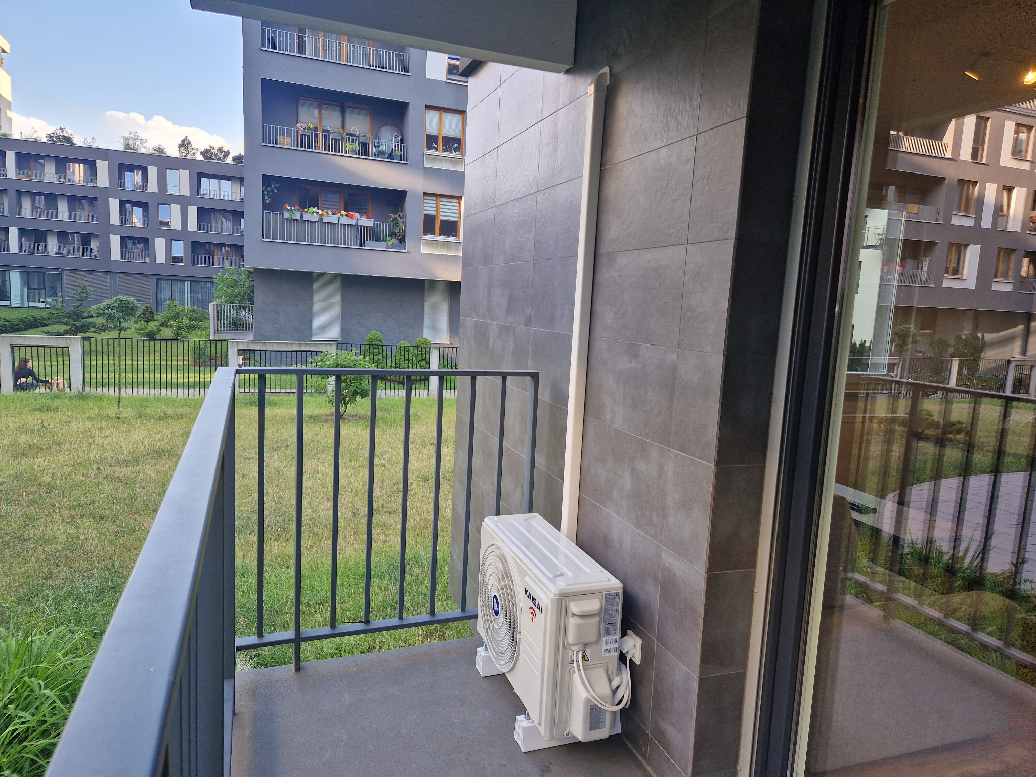 Jednostka zewnętrzna klimatyzacji Kasai zamontowana na balkonie nowoczesnego budynku mieszkalnego, widoczna zza barierki.