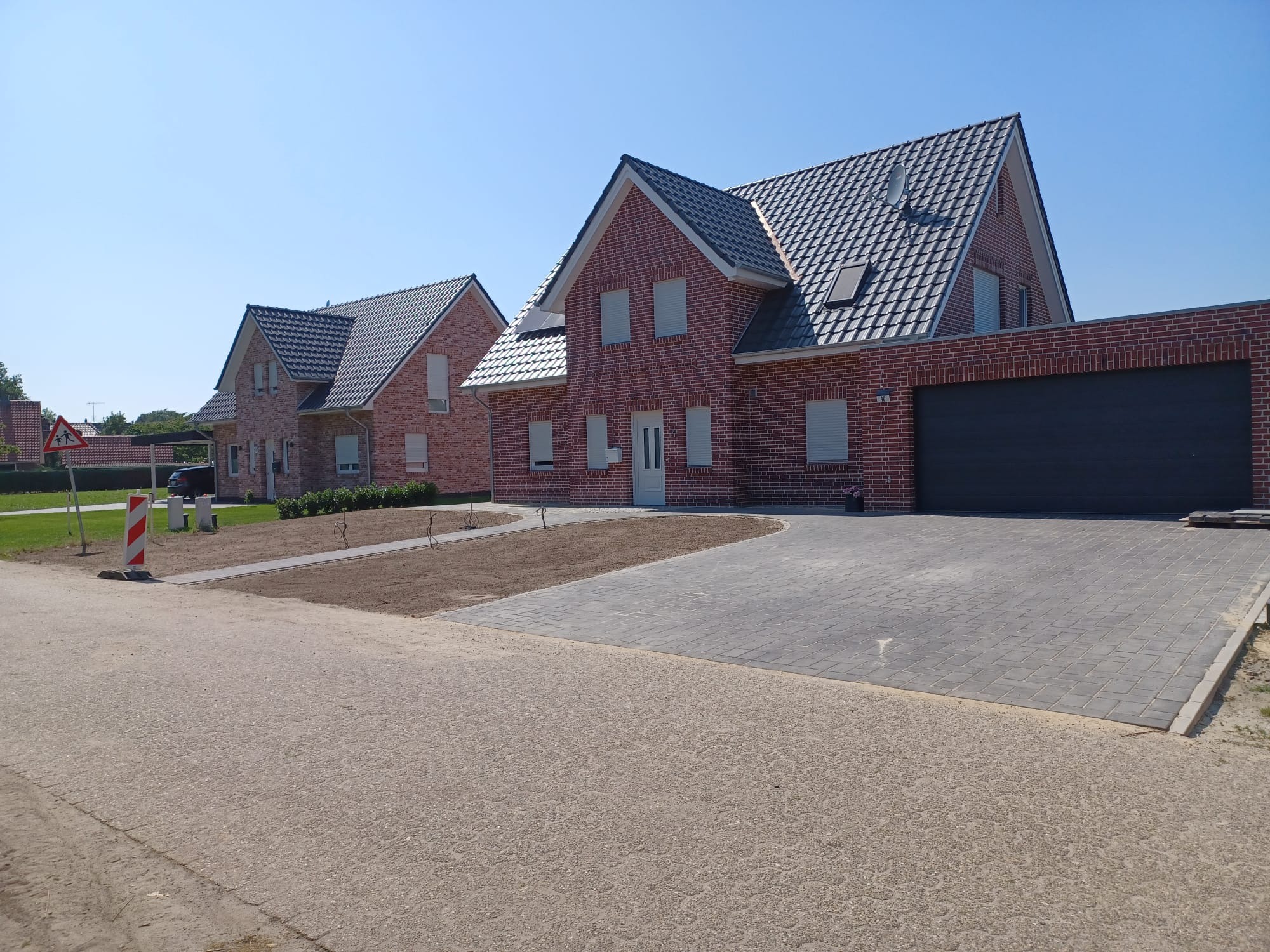 Nowoczesny dom z czerwonej cegły z szarym brukowanym podjazdem i zagospodarowanym terenem zielonym przed budynkiem.