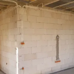 Wnętrze surowego domu w trakcie prac, widoczne białe ściany z betonu komórkowego, zamontowane przewody elektryczne w peszlach i pomarańczowe puszki instalacyjne pod gniazdka i włączniki, sufit...