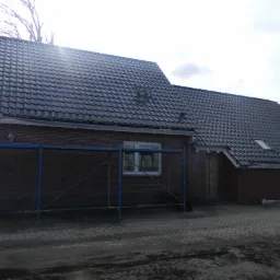 Częściowo wymienione, ciemne dachówki na dachu domu z czerwonej cegły, widoczne rusztowanie i fragment niezakończonej połaci dachu z lukarną.