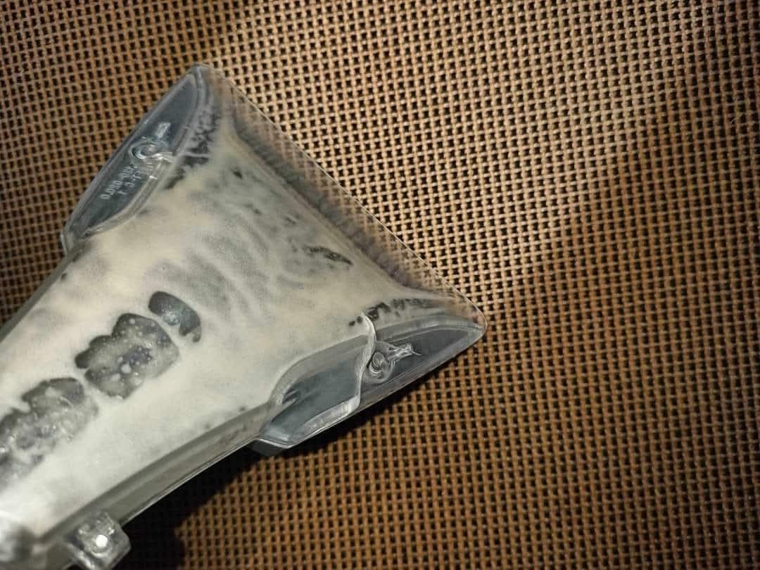 Przezroczysta końcówka odkurzacza piorącego z resztkami piany na tle brązowej, plecionej tkaniny.