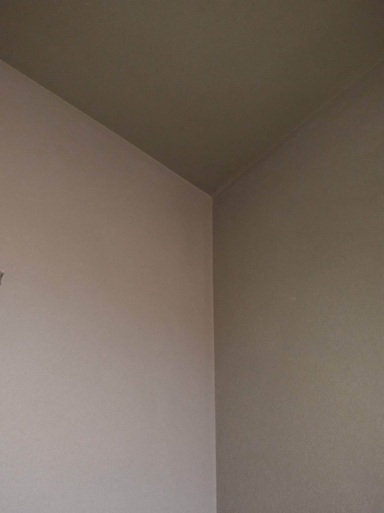 Pomieszczenie po malowaniu ścian i sufitu na dwa odcienie szarości, widoczny narożnik ściany i sufitu.