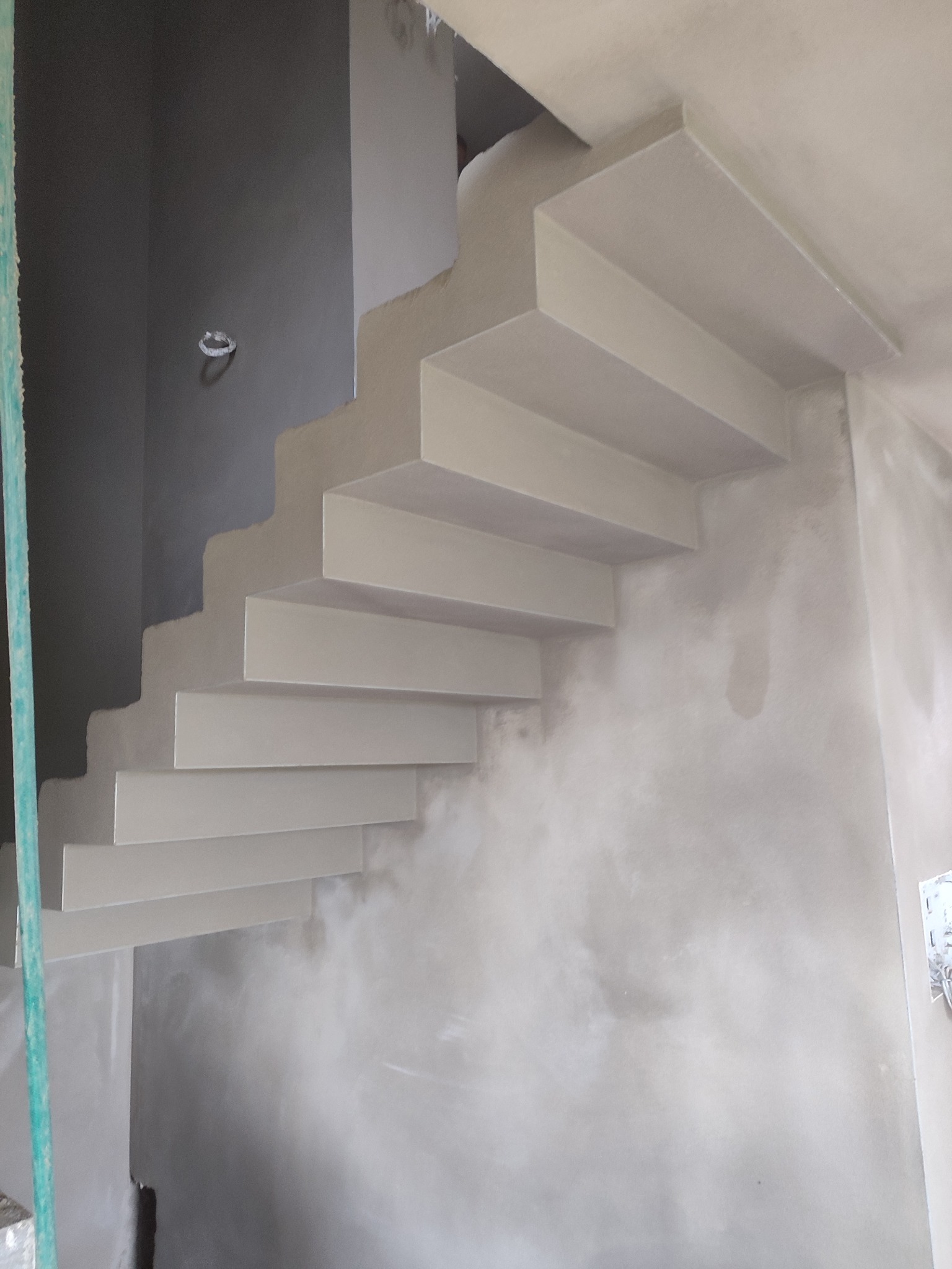 Betonowe schody wewnętrzne w surowym stanie, przed wykończeniem, z widocznymi śladami tynku na ścianach.