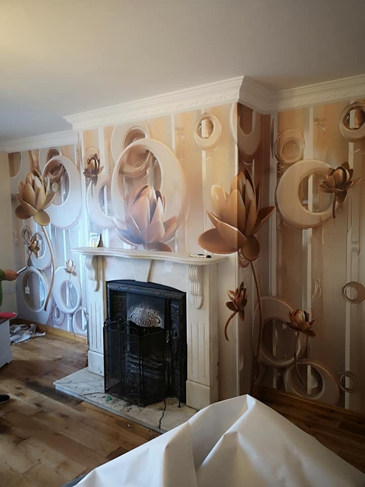 Ściana po tapetowaniu z motywem kwiatowym 3D, widoczny kominek z marmurową obudową i zabezpieczona podłoga.