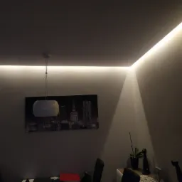 Nowoczesne oświetlenie sufitowe LED w salonie z obrazem panoramy miasta na ścianie, widoczne lampy wiszące i dekoracje.