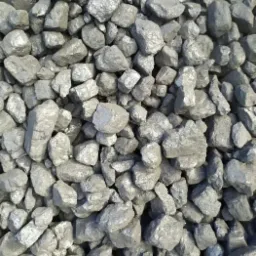 Kupa błyszczącego ekogroszku o nieregularnych kształtach, z widocznymi refleksami światła na powierzchni bryłek.