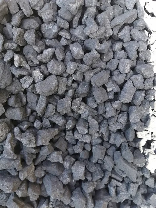 Kupa brył grafitowego opału o nieregularnych kształtach, oświetlona z prawej strony, ukazująca teksturę i matową powierzchnię poszczególnych kawałków.