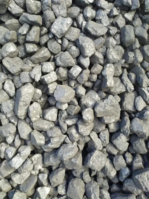 Kupa błyszczącego ekogroszku o nieregularnych kształtach, z widocznymi refleksami światła na powierzchni bryłek.