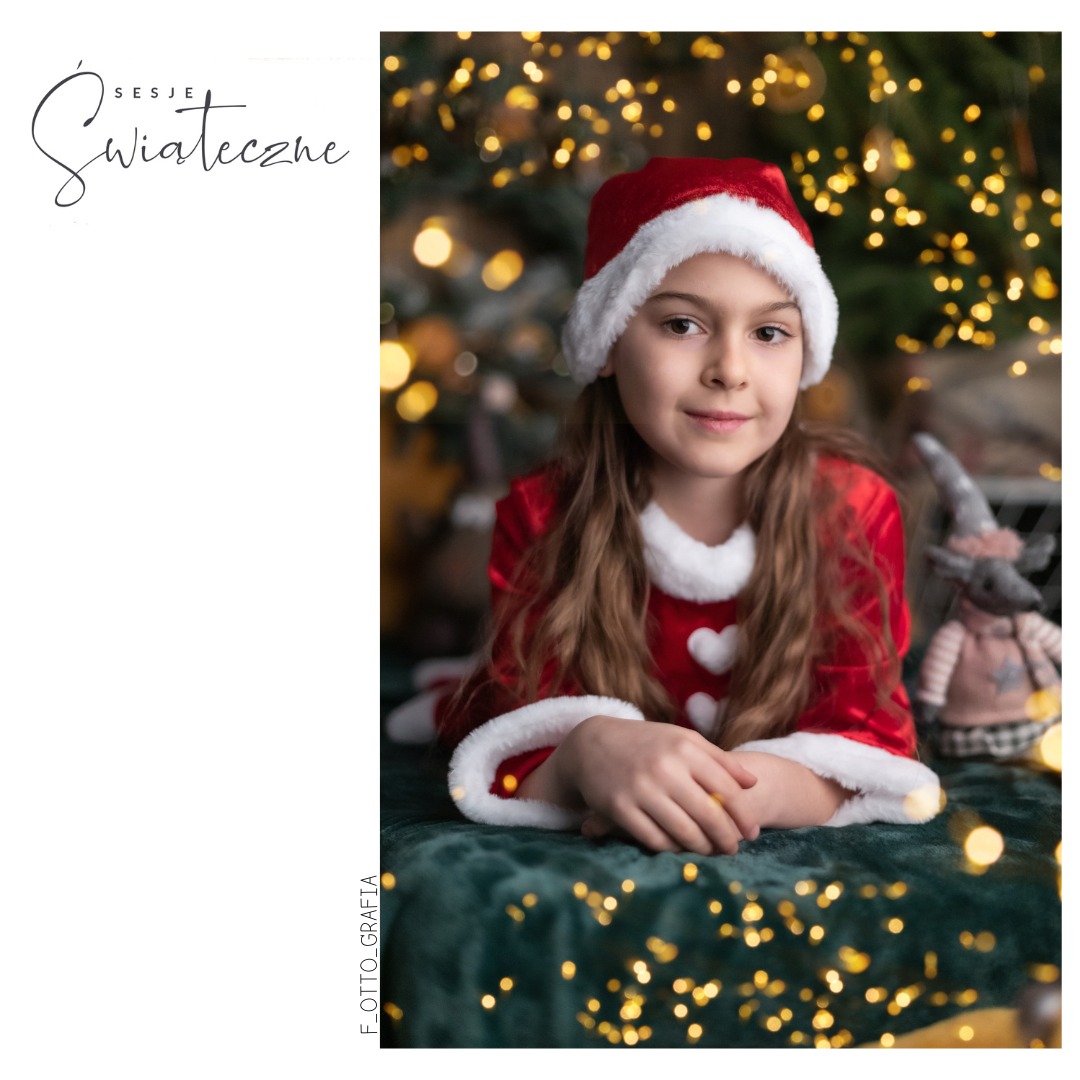 Dziewczynka w stroju Mikołaja leży na zielonym tle z lampkami, obok pluszowy skrzat. Uśmiechnięta, świąteczna atmosfera, delikatne oświetlenie.