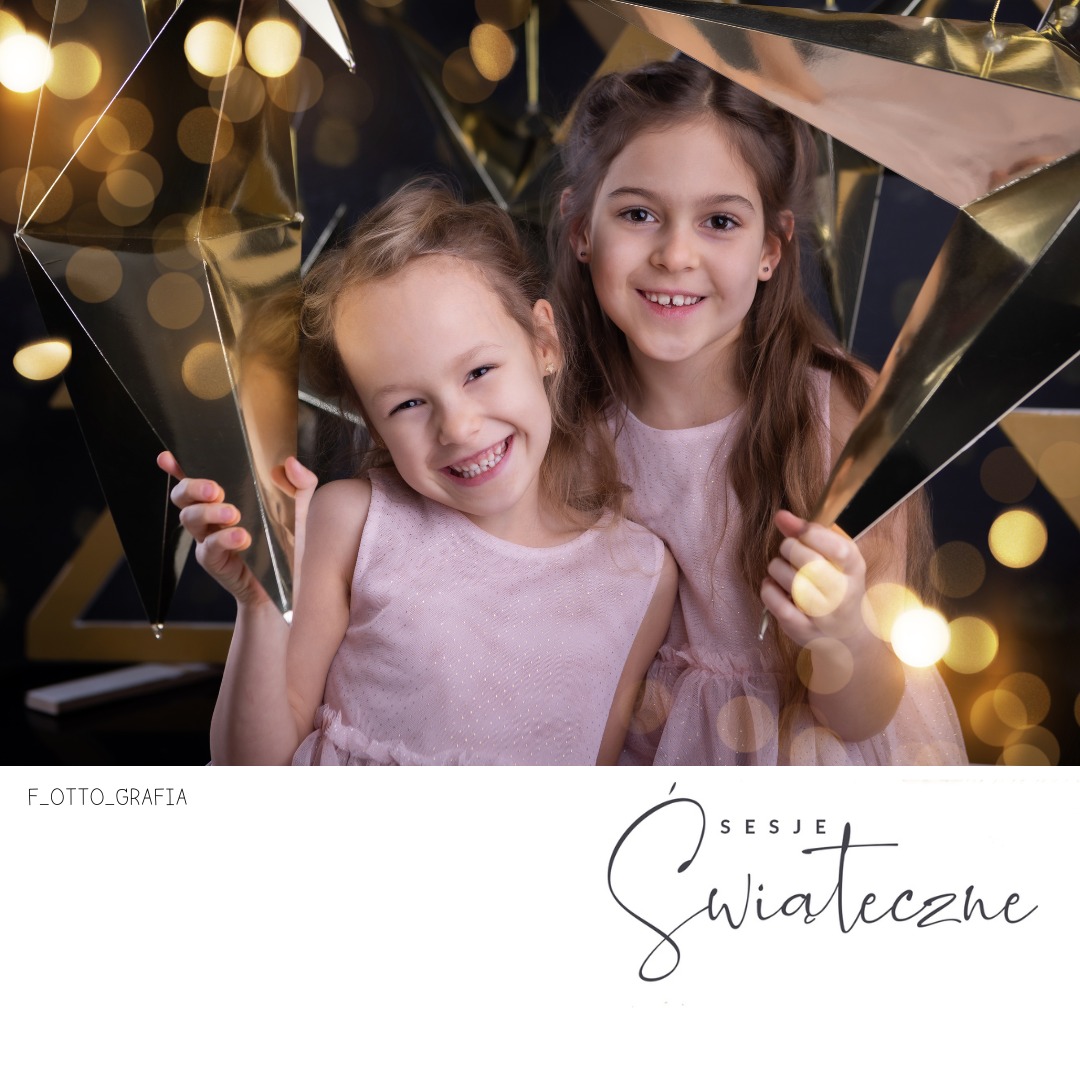 Dwie uśmiechnięte dziewczynki w różowych sukienkach pozują z dekoracjami w kształcie złotych gwiazd na tle światełek bokeh.