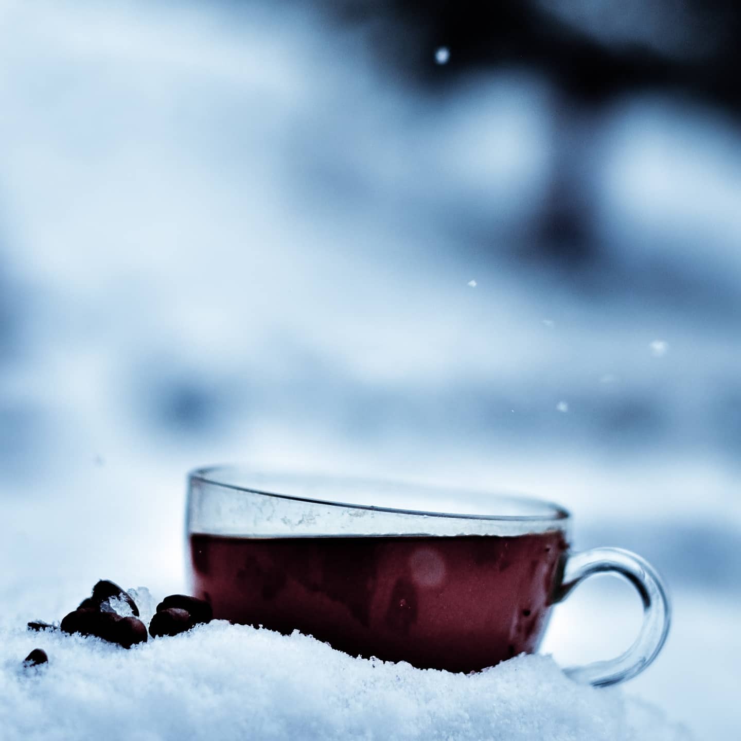 Szklanka z czerwonym płynem stoi na śniegu obok ziaren kawy, z rozmytym, zimowym tłem.