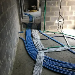 Instalacja elektryczna w surowym stanie: wiązki niebieskich i szarych peszli ułożone na podłodze, prowadzone do puszek w ścianach z betonu komórkowego.