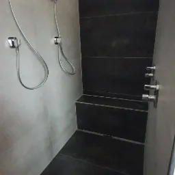 Nowoczesna kabina prysznicowa z szarymi ścianami, ciemnymi płytkami i dwoma słuchawkami prysznicowymi oraz deszczownicą.