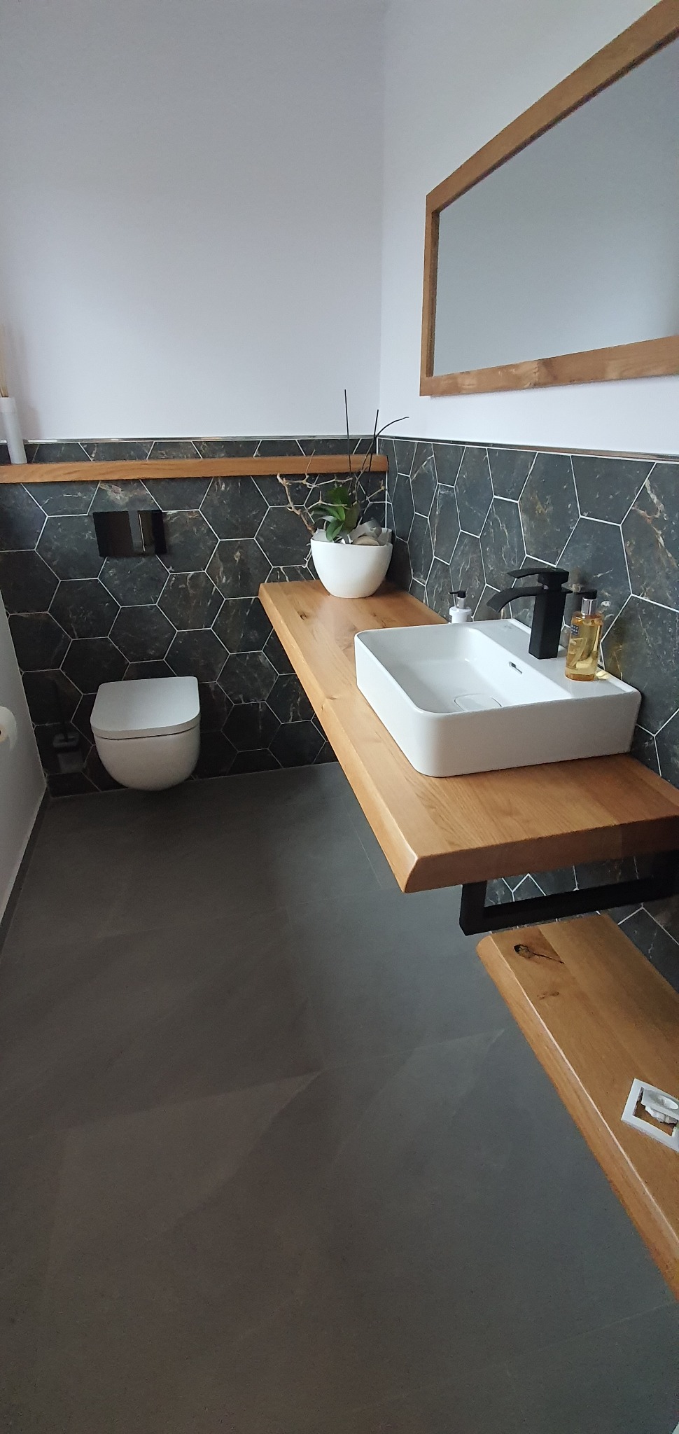 Nowoczesna łazienka z heksagonalnymi płytkami w odcieniach szarości, drewnianym blatem pod umywalką nablatową i wiszącą toaletą