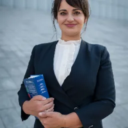 Uśmiechnięta kobieta w ciemnym garniturze i białej bluzce z falbanami, trzymająca w rękach niebieską książkę z napisem 'Edycja Sądowa' i skrótami KSH, KRSU, MSiGU, PrUpad, na tle jasnej...