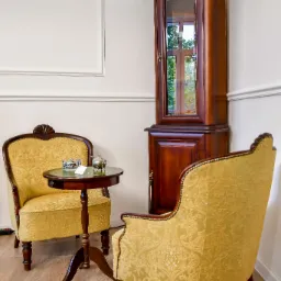 Antyczne fotele z wzorzystą tapicerką, stolik z dekoracjami i witryna w rogu pokoju. Klasyczny wystr&oacute;j wnętrza z drewnianą podłogą.