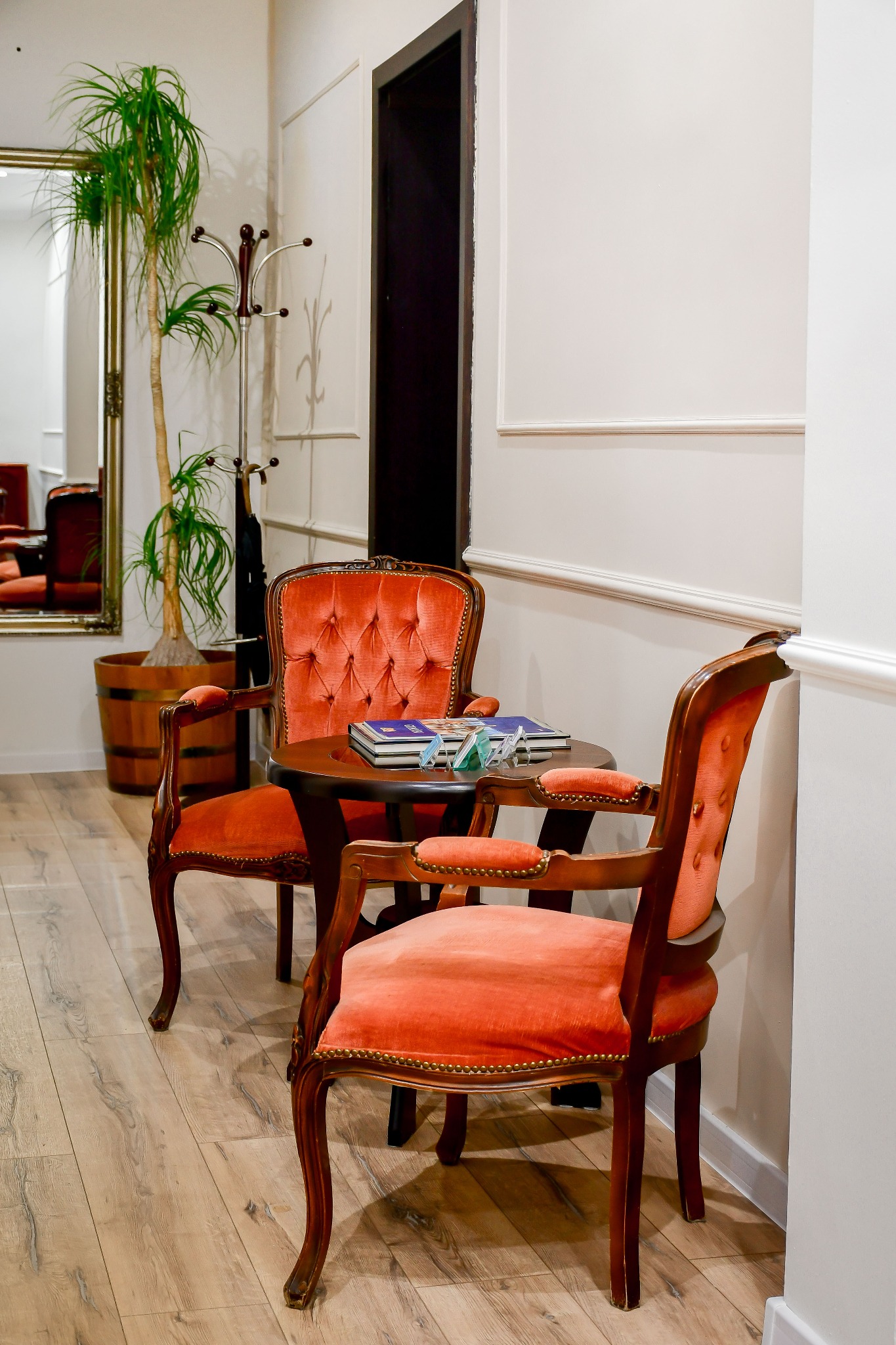 Eleganckie krzesła z pomarańczową tapicerką i drewnianymi ramami przy okrągłym stoliku w jasnym wnętrzu kancelarii, z podłogą imitującą drewno.