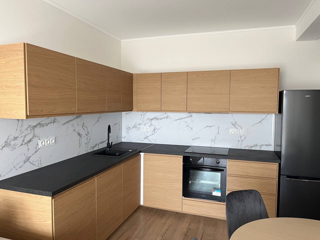Nowoczesna kuchnia z drewnianymi szafkami i marmurowym backsplash we Wrocławiu. Czarny blat i sprzęt AGD. Minimalistyczny design, jasne wnętrze.