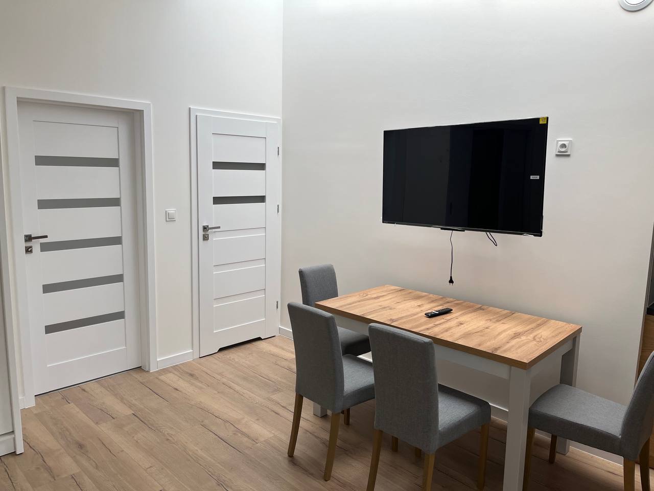 Jasne wnętrze po remoncie: dwie białe, nowoczesne drzwi z poziomymi przeszkleniami, stół z krzesłami i telewizor na ścianie. Parkiet w odcieniach drewna.
