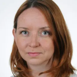 Portret kobiety o rudych włosach i zielonych oczach, na białym tle, z delikatnym uśmiechem.