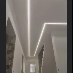 Korytarz w trakcie remontu z zamontowanym oświetleniem LED w suficie podwieszanym, widoczne niedokończone ściany i podłoga z pozostałościami po pracach.