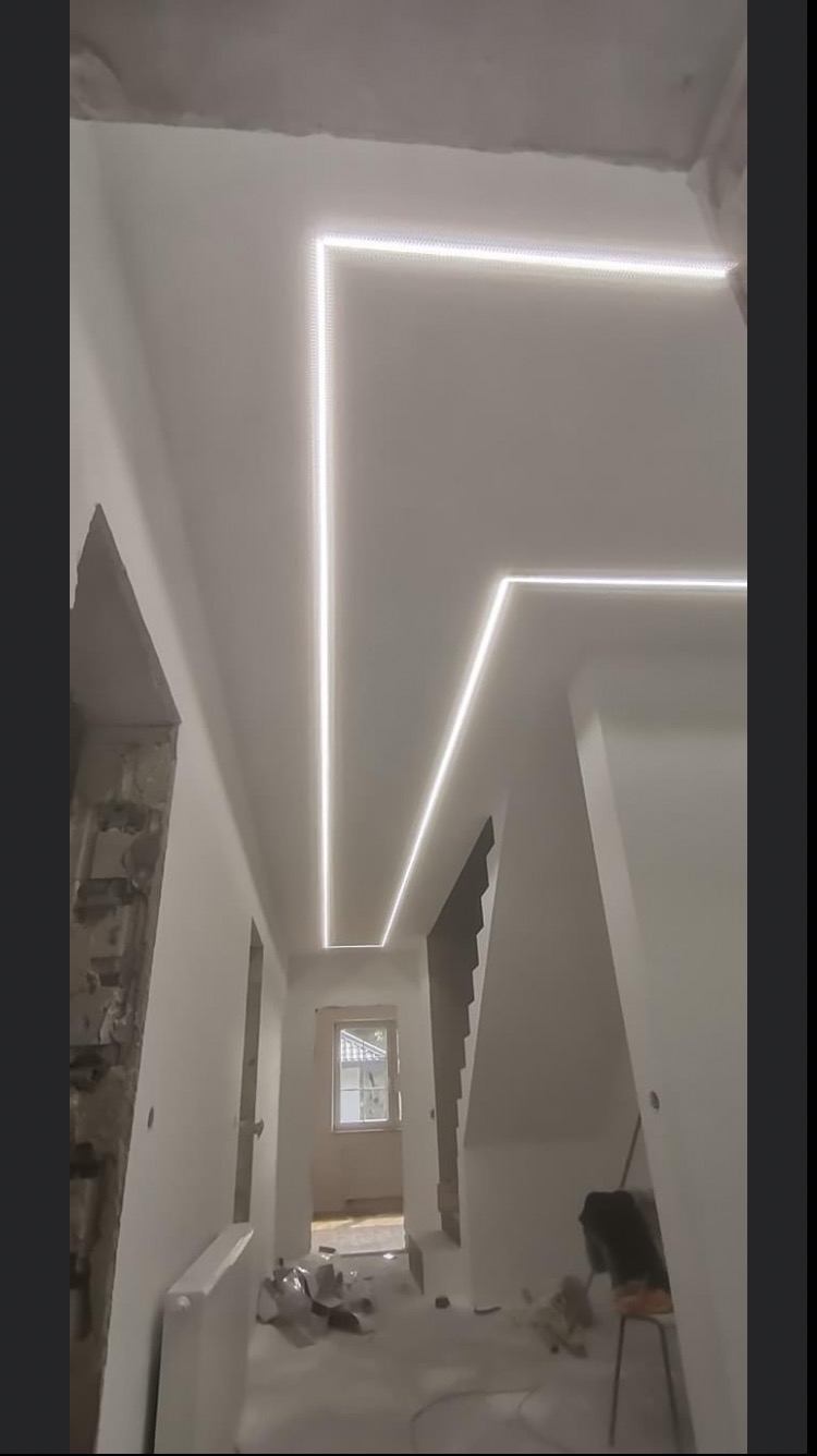 Korytarz w trakcie remontu z zamontowanym oświetleniem LED w suficie podwieszanym, widoczne niedokończone ściany i podłoga z pozostałościami po pracach.