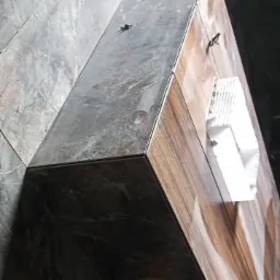 Wykończona obudowa wnęki z płytek imitujących drewno i marmur, widoczny narożnik z listwą wykończeniową i fragment ściany wyłożonej płytkami marmuropodobnymi.