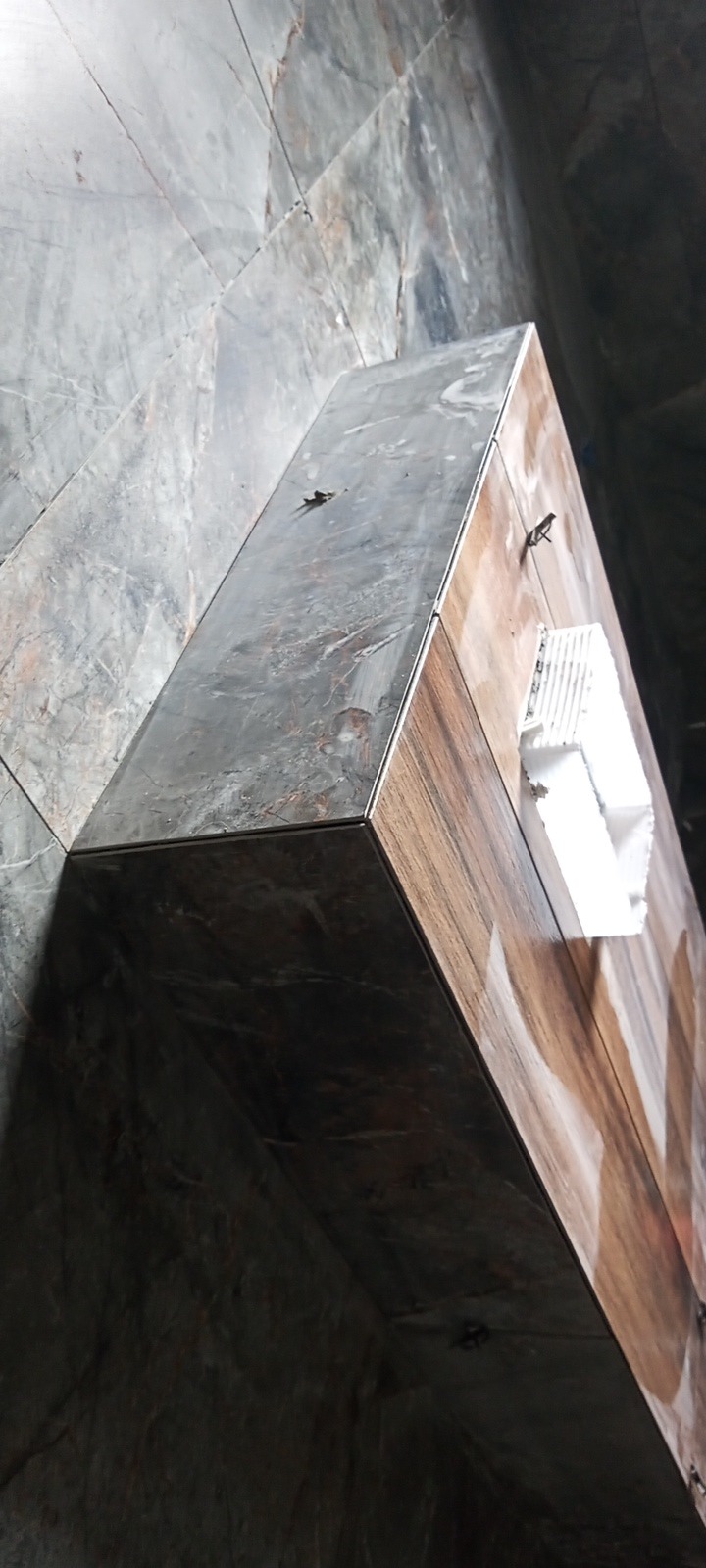 Wykończona obudowa wnęki z płytek imitujących drewno i marmur, widoczny narożnik z listwą wykończeniową i fragment ściany wyłożonej płytkami marmuropodobnymi.