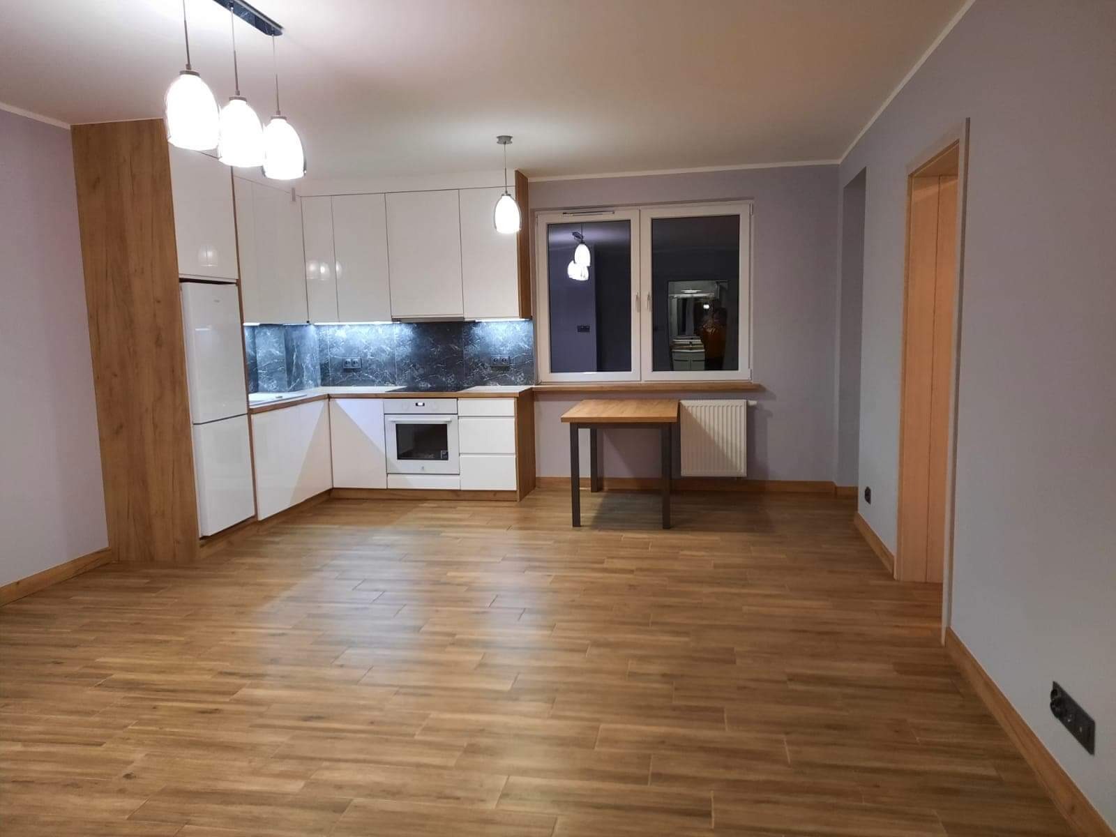 Nowoczesna kuchnia z białymi szafkami, marmurkowym backsplashiem, drewnianymi akcentami i stołem w nowym mieszkaniu.