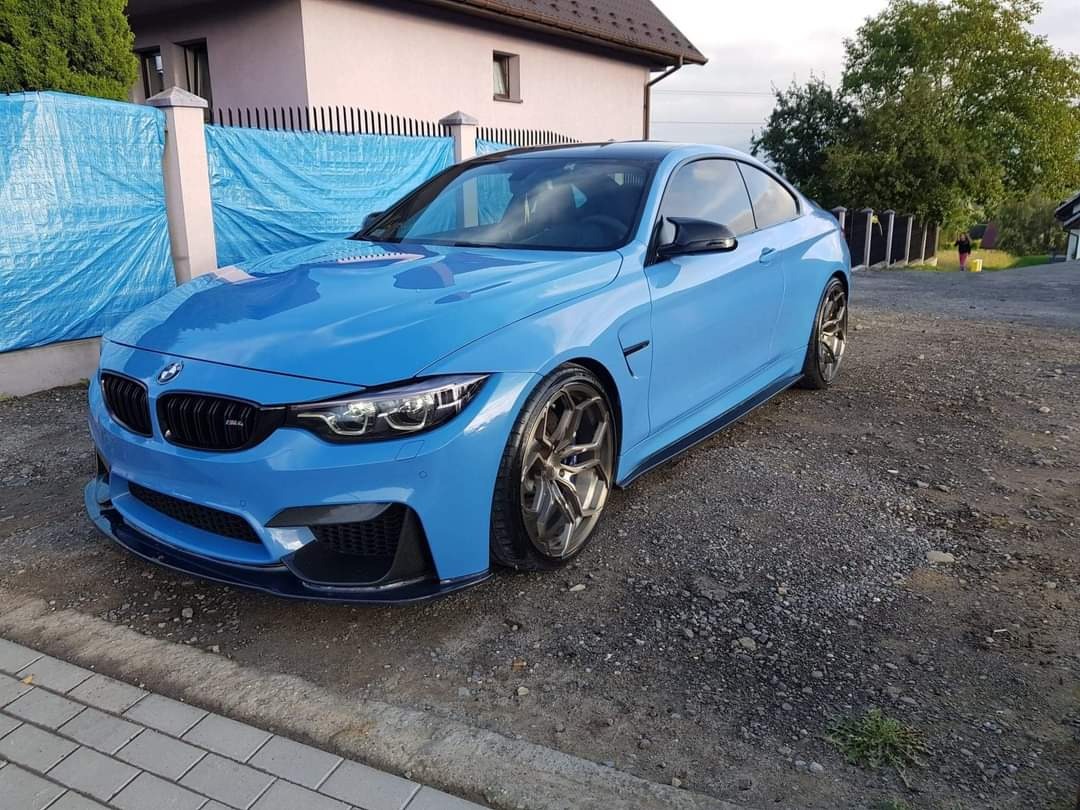 Błękitne BMW M4 po renowacji lakieru, zaparkowane na żwirowym podjeździe, widoczne detale: czarne felgi i karbonowy splitter.