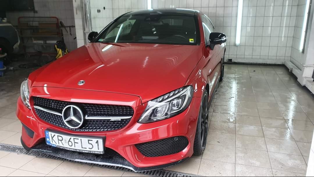 Czerwony Mercedes-Benz klasy C po umyciu w myjni, widoczne mokre płytki posadzkowe, czarne felgi i tablica rejestracyjna KR 6FL51.
