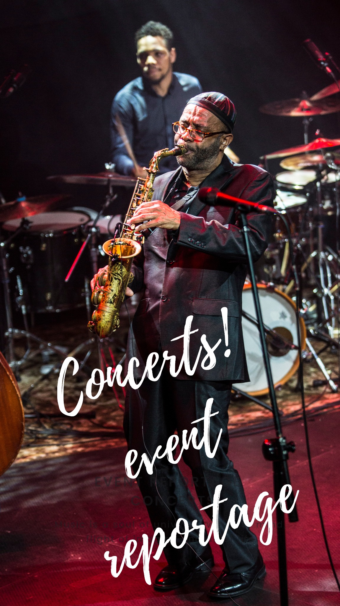 Saksofonista w czarnym garniturze i czapce gra na saksofonie na scenie z perkusistą w tle, oświetlony czerwonym światłem.