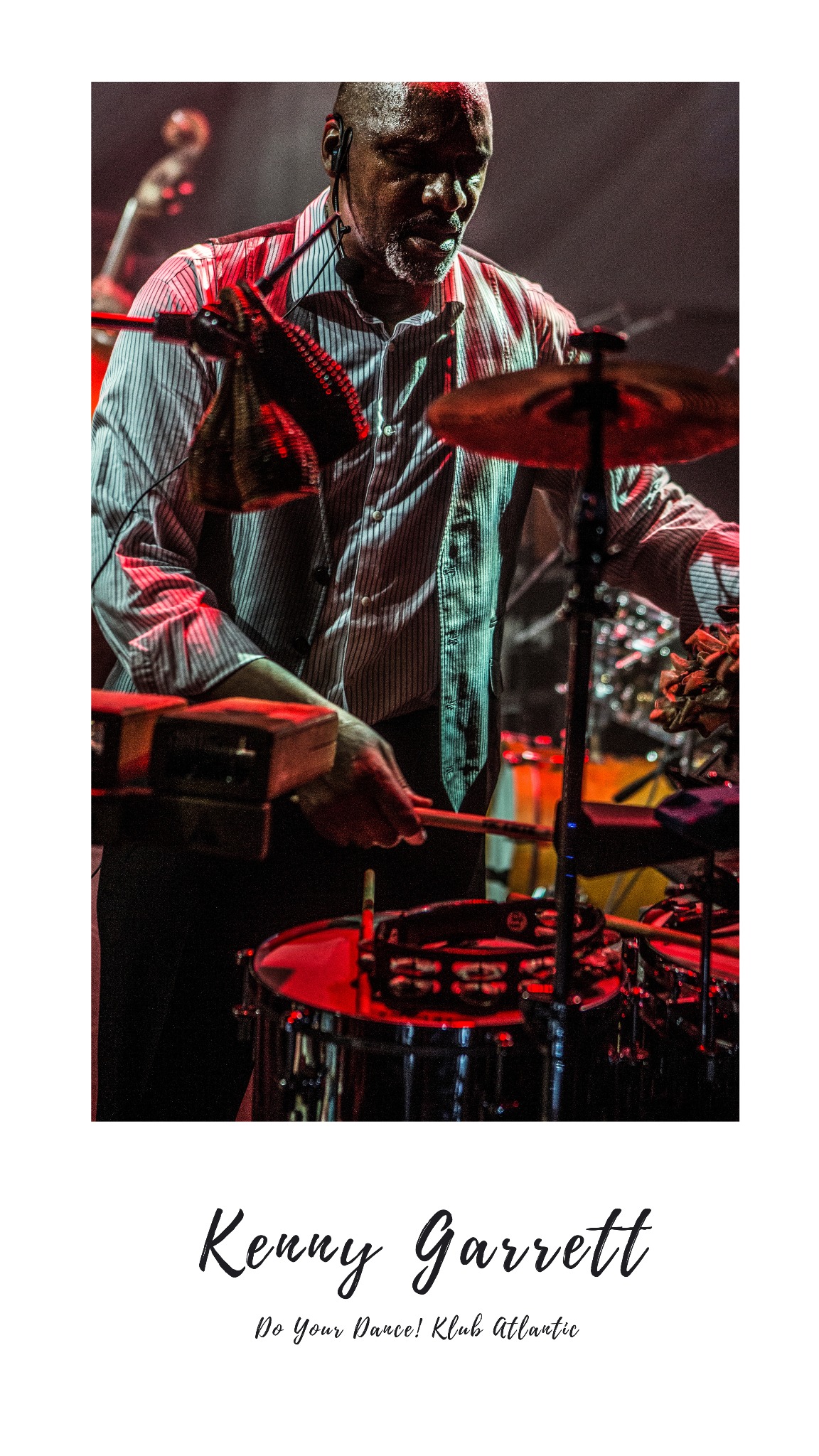 Perkusista w paski gra na perkusji i cowbell podczas występu na żywo, oświetlony czerwonym światłem scenicznym.