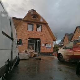 Henryk Jasiak Usługi Budowlane - Budynek w trakcie budowy z cegły z dachem krytym strzechą, widoczne rusztowania i materiały budowlane, pochmurne niebo.
