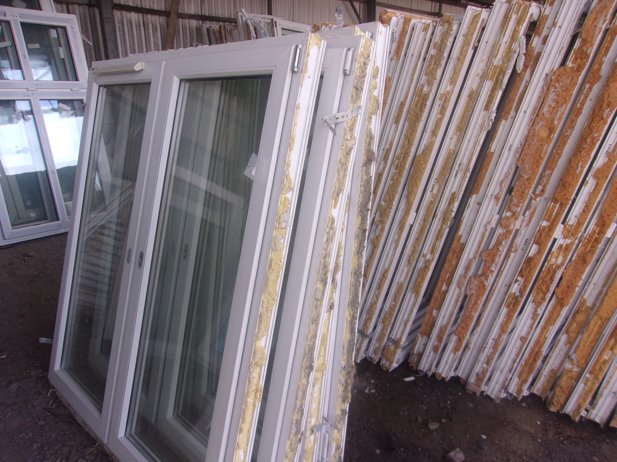 Magazynowane białe ramy okienne z widocznymi uszczelkami i elementami montażowymi, ułożone jedne na drugich, czekające na montaż.