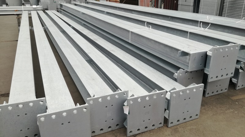 Srebrne, ocynkowane profile stalowe w kształcie litery I, przygotowane do montażu, z widocznymi otworami na śruby w podstawach.