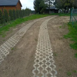 Ścieżka z ażurowych płyt betonowych prowadząca do zabudowań w Krotoszynie, widok z bliska na ułożoną nawierzchnię z widoczną ziemią i trawą w otworach płyt.