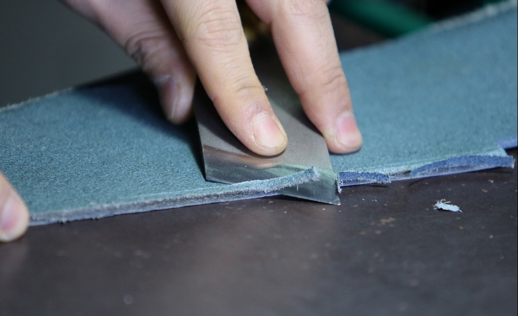 Przycinanie krawędzi szarego materiału nożem introligatorskim na ciemnym blacie.