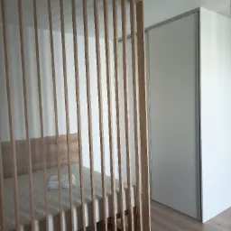 Drewniana ażurowa ścianka działowa oddzielająca łóżko od szafy przesuwnej w minimalistycznym wnętrzu.