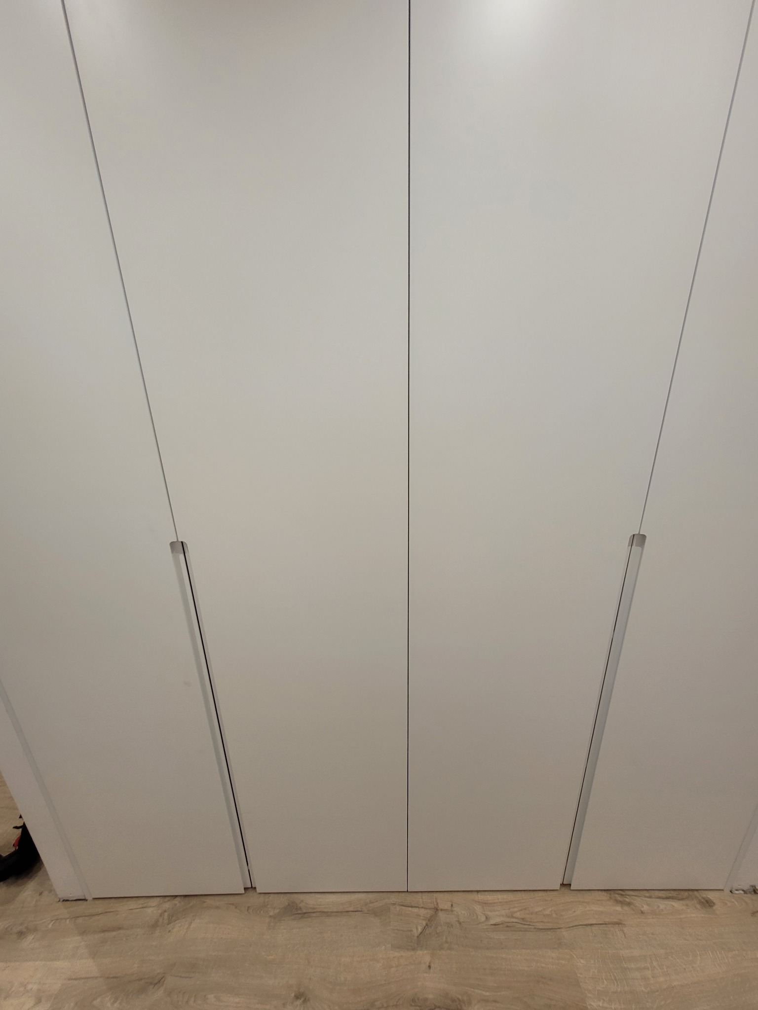 Minimalistyczna, biała szafa z ukrytymi uchwytami, idealnie wpasowana w jasne wnętrze. Widoczna struktura drewnianej podłogi dodaje ciepła.