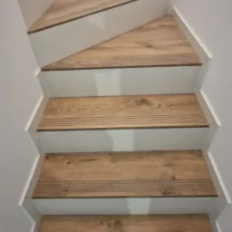 Schody wewnętrzne wyłożone panelami imitującymi drewno, z białymi podstopnicami i listwami przypodłogowymi, widok z góry.