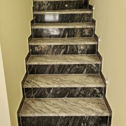 Ekipa Alana - Schody wyłożone marmurem w odcieniach szarości i czerni, z podświetleniem LED na ścianie, widoczne zabezpieczenia podłogi.