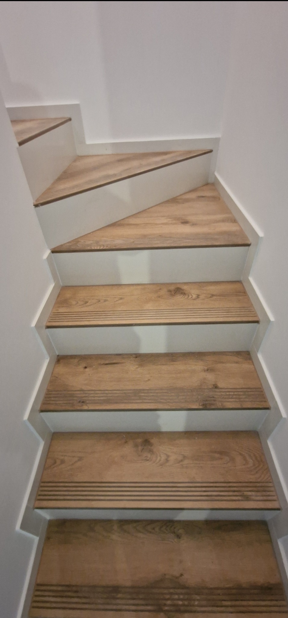 Schody wewnętrzne wyłożone panelami imitującymi drewno, z białymi podstopnicami i listwami przypodłogowymi, widok z góry.